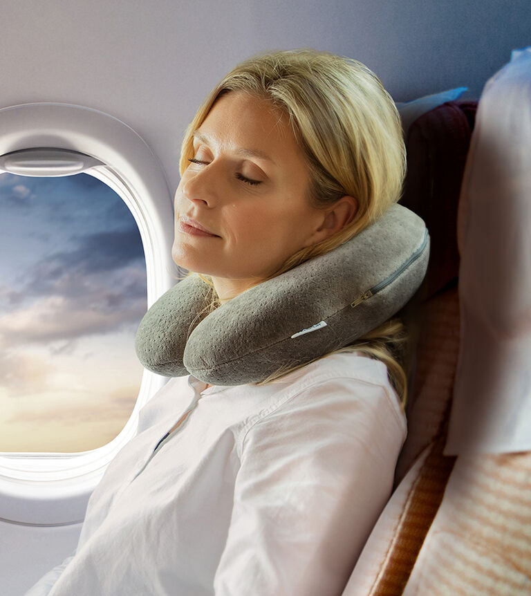 kobieta śpi w samolocie mając na szyi specjalną poduszkę do spania w czasie podróży