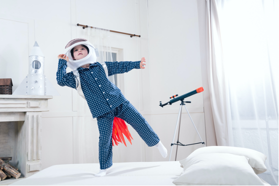 dziecko w stroju kosmonauty skacze po łóżku